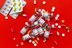 Array of COVID-19 vaccine vials and various pills on a vibrant red surface, showcasing medicine and healthcare themes.